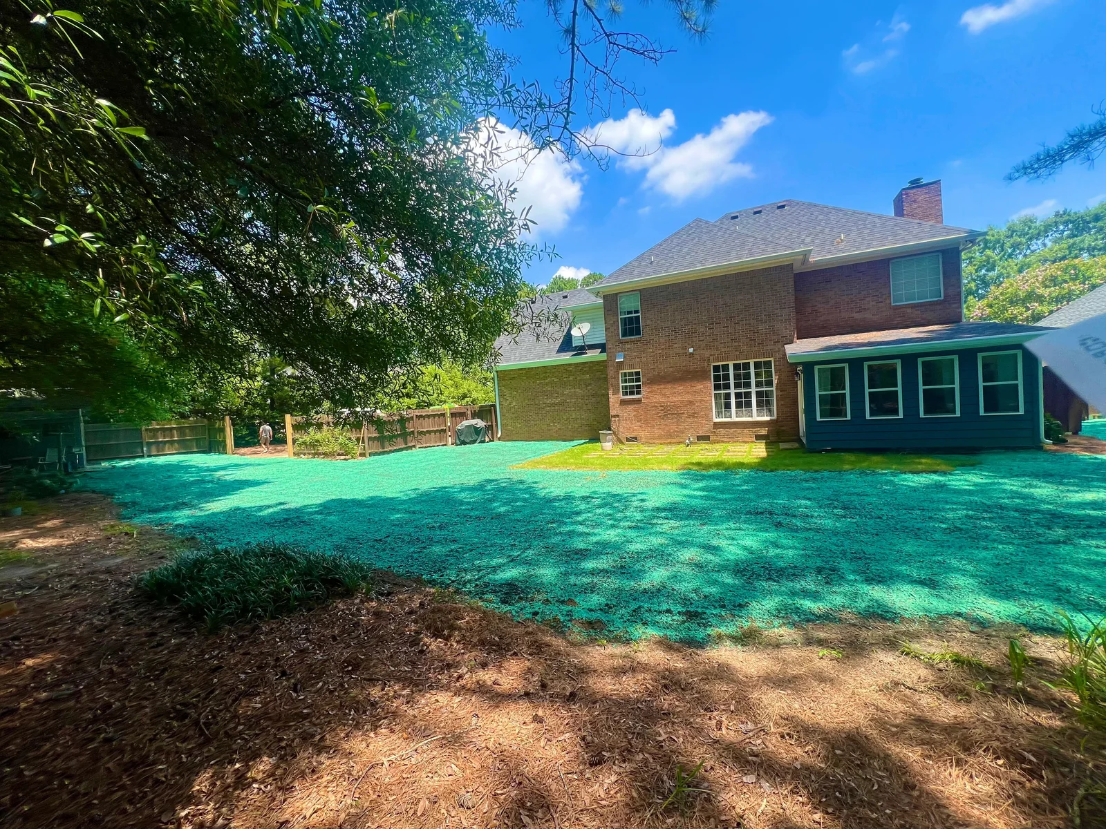 Freshly installed sod covering a residential front lawn in Aiken, SC, with clean-cut edges along a concrete driveway and green turf laid in tight, uniform rows. A landscaping crew from Greenhold Co. works in the background, grading and placing sod sections across the prepared soil.